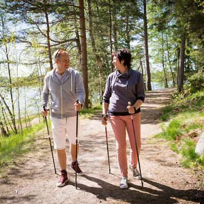 Bild vergrößern: Ein Mann und eine Frau gehen mit Nordic Walking-Stcken auf einem Sandweg.