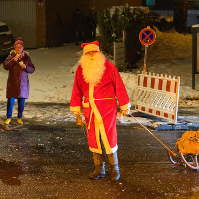 Bild vergrößern: Ein Weihnachtsmann steht auf einer Straße und zieht einen Schlitten hinter sich her.