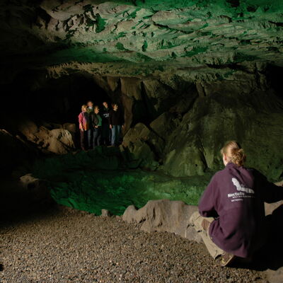 Bild vergrößern: Eine Hhlenfhrerin zeigt einer Gruppe die beleuchtete Kalkberghhle.