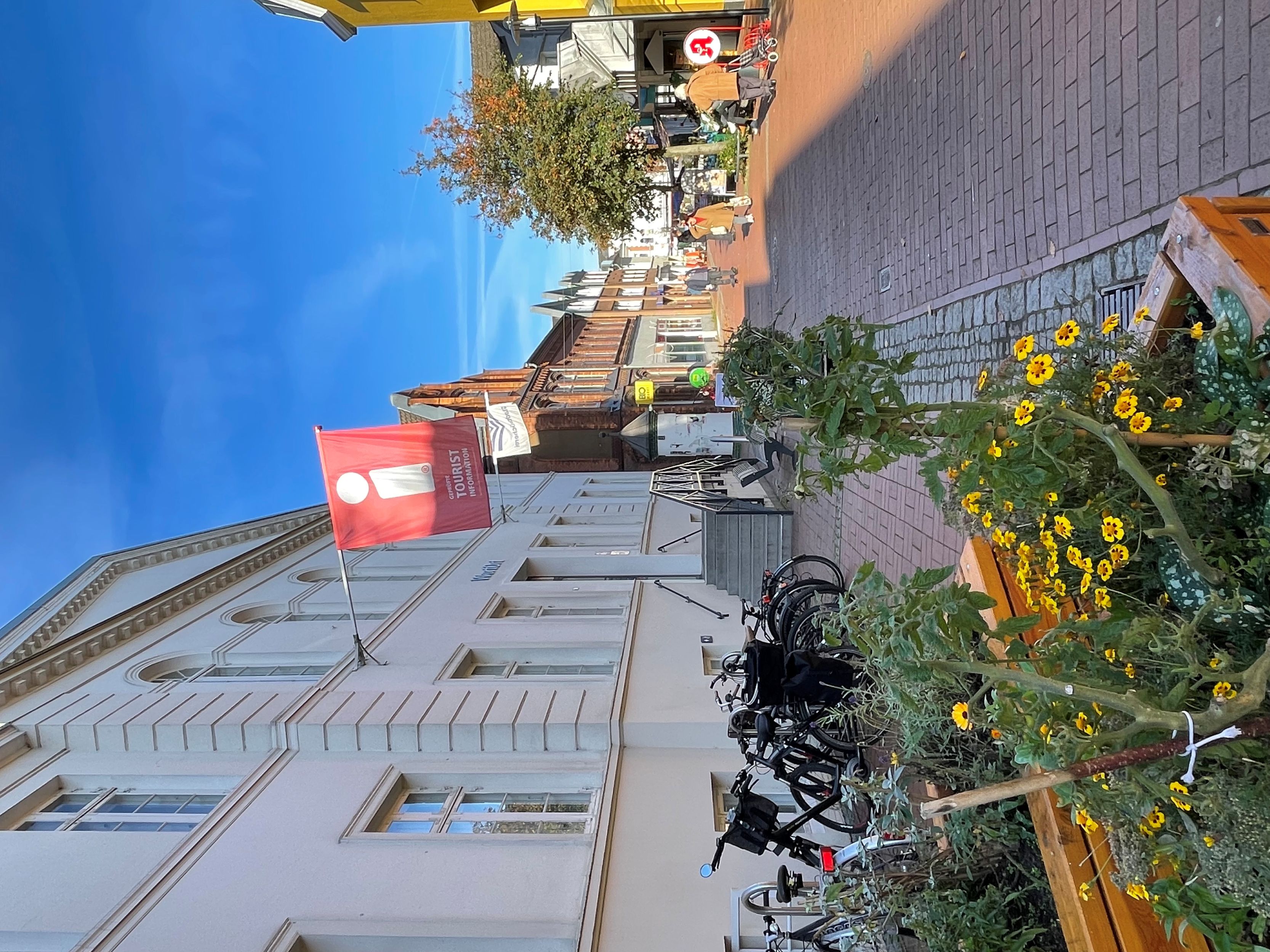 Straße in Bad Segeberg mit Fahrradständern, Blumenbeeten und einem roten Tourist-Informationsschild an einem weißen Gebäude