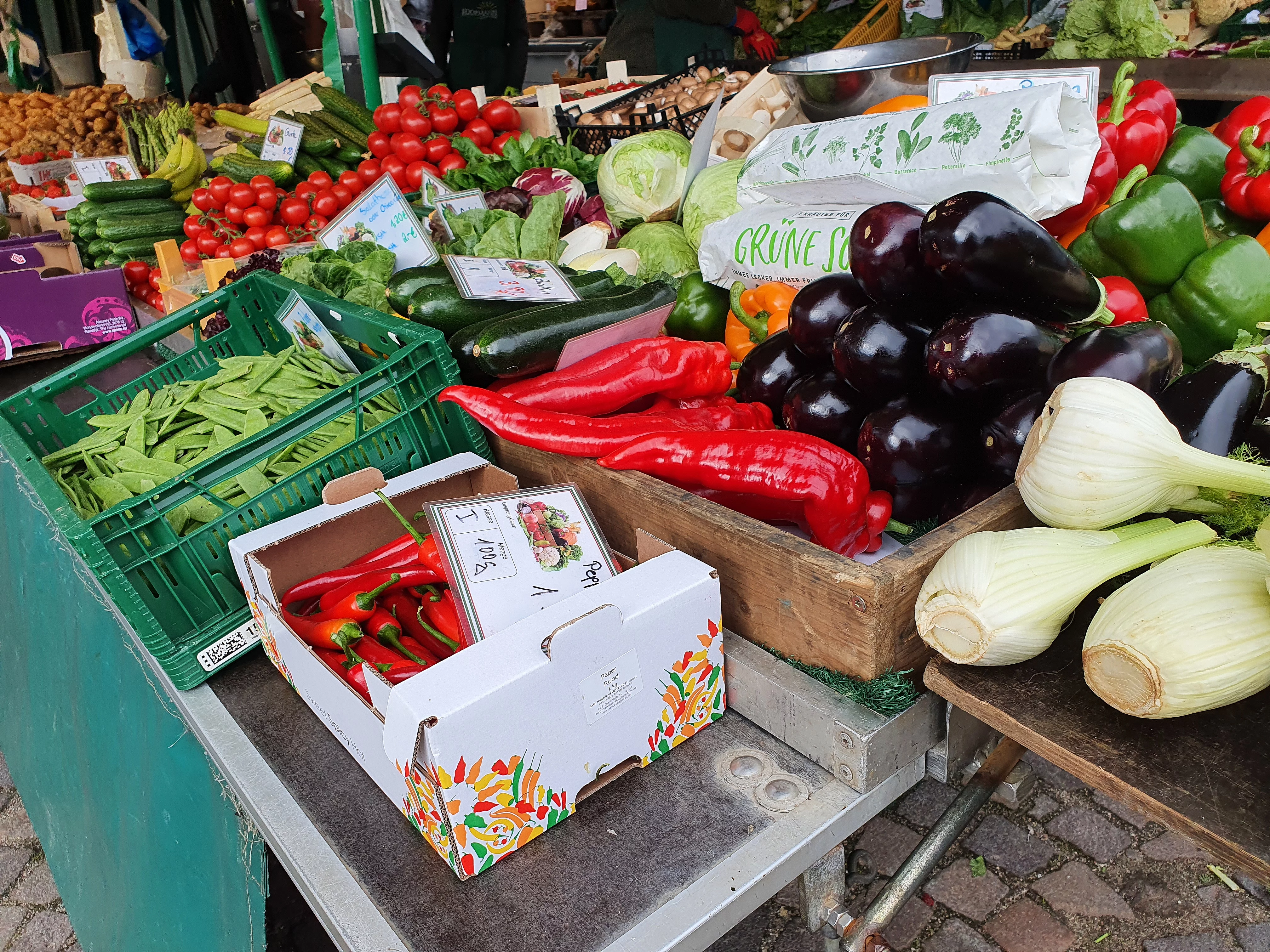 Marktstand mit verschiedenen frischen Gemüsesorten wie Paprika, Auberginen, Fenchel und Tomaten auf Holzkisten und in Kartons