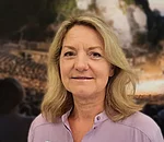 Frau mit schulterlangem, gewelltem blonden Haar trägt ein helles Hemd mit Stehkragen vor unscharfem Hintergrund