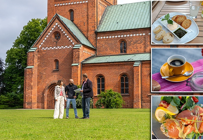 Drei Personen stehen auf einer Wiese vor einer großen Backstein-Kirche mit grünem Dach