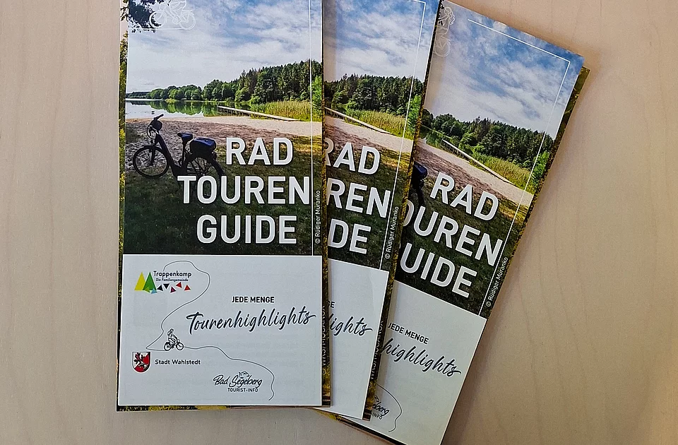 Mehrere gefaltete Rad- und Wanderkarten sowie ein Radtourenguide liegen auf einem hellen Untergrund