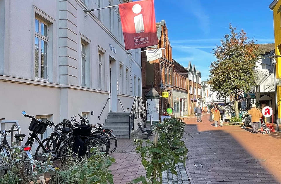 Straße in Bad Segeberg mit Fahrradständern, Blumenbeeten und einem roten Tourist-Informationsschild an einem weißen Gebäude