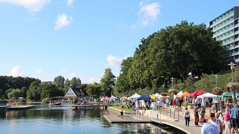 Uferpromenade mit Menschen, bunten Zelten und Bäumen am See beim Seefest Bad Segeberg