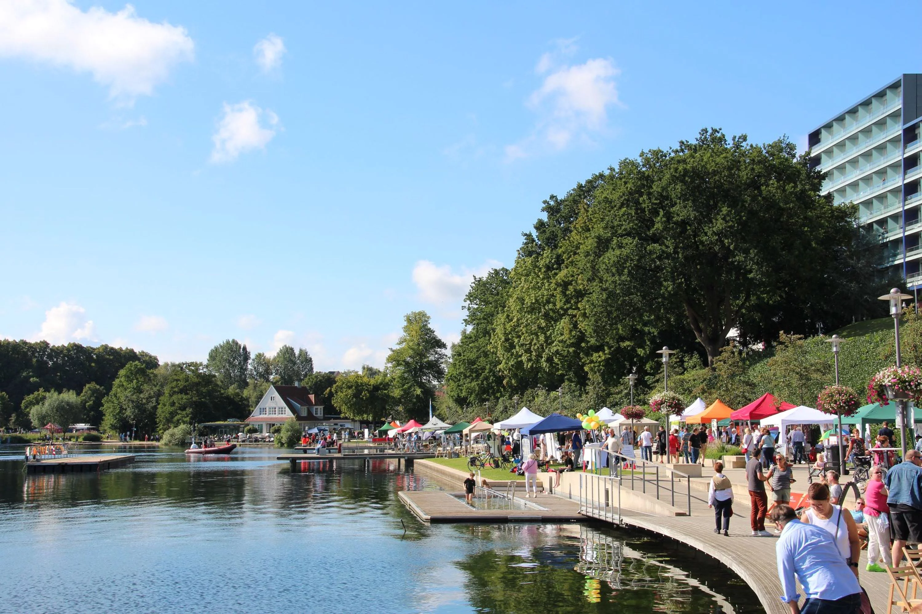 Uferpromenade mit Menschen, bunten Zelten und Bäumen am See beim Seefest Bad Segeberg