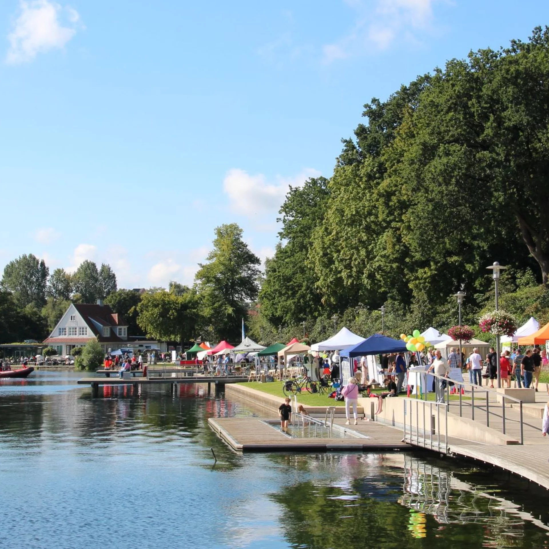 Uferpromenade mit Menschen, bunten Zelten und Bäumen am See beim Seefest Bad Segeberg