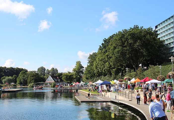 Uferpromenade mit Menschen, bunten Zelten und Bäumen am See beim Seefest Bad Segeberg