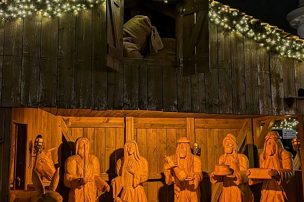 Krippenszene mit hölzernen Figuren von Maria, Josef, den Heiligen Drei Königen und weiteren Personen vor einer beleuchteten Holzhütte mit einem roten Stern darüber