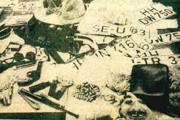 Tisch mit verschiedenen Beweismitteln darunter mehrere Nummernschilder, eine Pistole, ein Hut und weitere Gegenstände