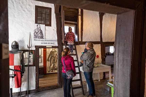 Familie mit zwei Kindern in einem historischen Fachwerkraum des Museums Segeberger Bürgerhaus mit Ritterrüstung und Holzleiter zu einer Empore