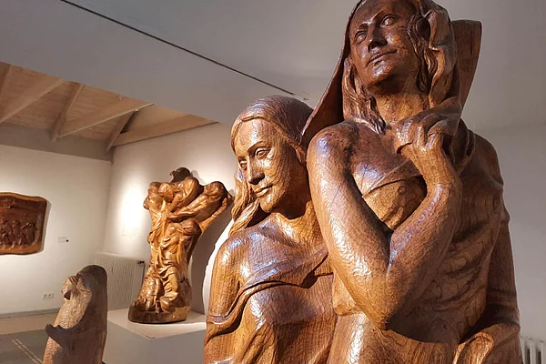 Holzskulpturen von Otto Flath in einem Ausstellungsraum mit sichtbaren Deckenbalken und weiß gestrichenen Wänden