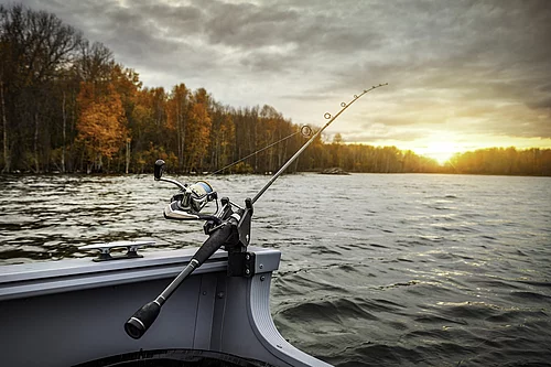 Angelrute in Halterung an einem Boot mit herbstlich gefärbtem Wald und Sonnenuntergang im Hintergrund