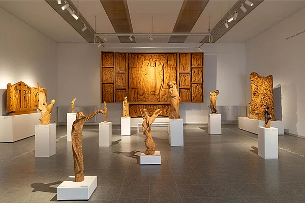 Ausstellungshalle der Kunsthalle Otto Flath Bad Segeberg mit mehreren hölzernen Skulpturen auf weißen Podesten und einem großen geschnitzten Holzrelief an der Rückwand