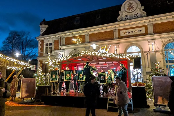Weihnachtsmarkt mit beleuchtetem Verkaufsstand vor einem historischen Gebäude bei Abenddämmerung