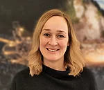 Frau mit schulterlangem, welligem Haar trägt schwarzen Pullover vor unscharfem Hintergrund