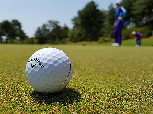 Nahaufnahme eines Golfballs der Marke Callaway auf dem Rasen mit zwei Golfern im Hintergrund