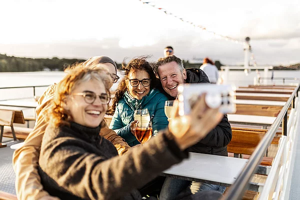 Gruppe von vier Personen sitzt auf einer Schifffahrt und macht Selfie mit Getränken auf einem Tisch