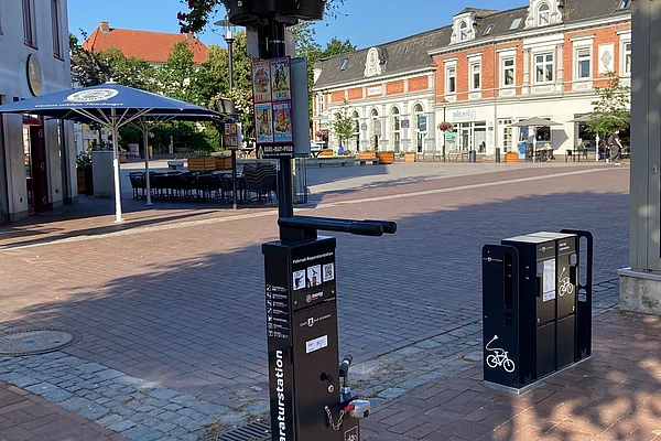 Schwarze Fahrradreparaturstation mit Werkzeugen an einem Laternenpfahl auf gepflastertem Marktplatz vor historischen Gebäuden