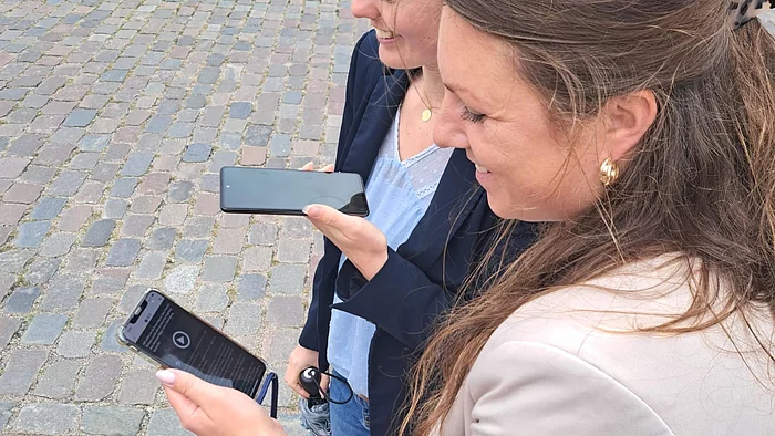 Zwei Frauen stehen auf einem gepflasterten Platz und halten Smartphones in den Händen