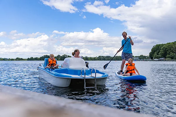Familie auf dem Großen Segeberger See mit Tretboot und Stand-up-Paddle-Board bei bewölktem Himmel