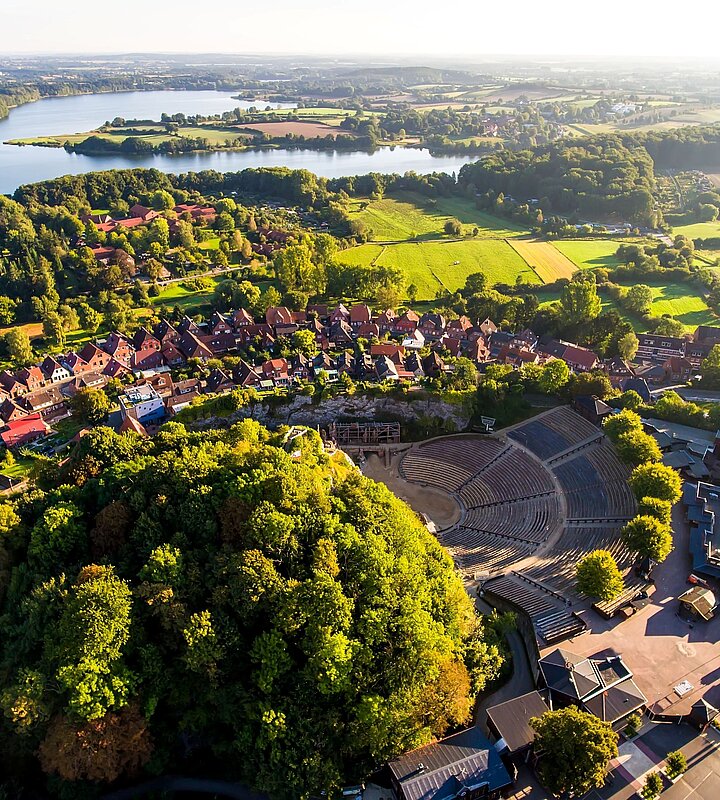 Luftaufnahme von Bad Segeberg mit dem Kalkberg, dem Freilichttheater und dem umliegenden See sowie der Stadt