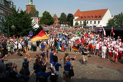 Große Menschenmenge auf einem Platz vor historischen Gebäuden, einige Personen schwenken deutsche Fahnen