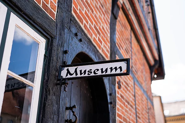  Schild mit der Aufschrift 'Museum' an einem Fachwerkhaus mit rotem Backstein und schwarzem Holzrahmen   