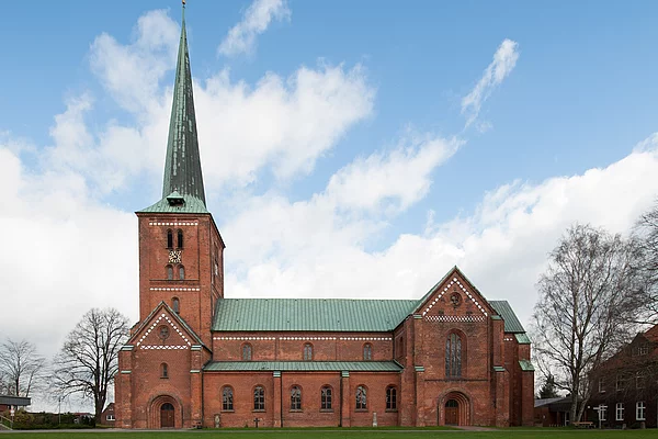 Marienkirche Bad Segeberg mit hohem spitzem Turm, rotem Backsteinmauerwerk und grünem Dach vor blauem Himmel