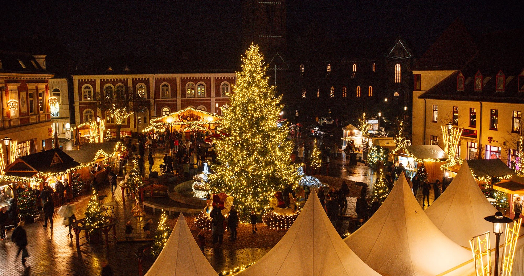 Weihnachtsmarkt in Bad Segeberg bei Nacht mit beleuchtetem großen Weihnachtsbaum, festlich geschmückten Ständen und Menschen auf dem Marktplatz