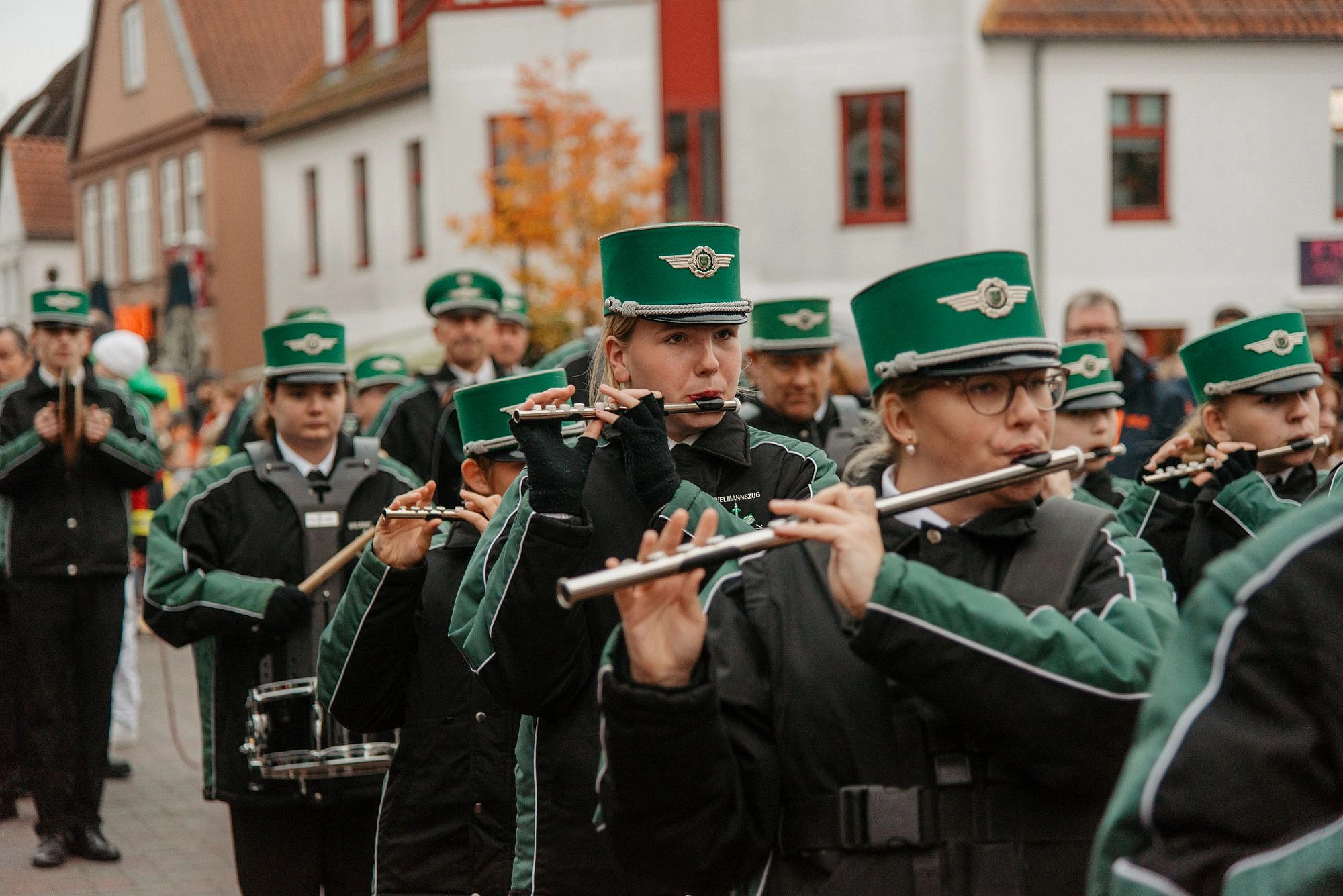 Mehrere Musiker in grünen Uniformen und Mützen spielen Querflöte in einer Straßenparade