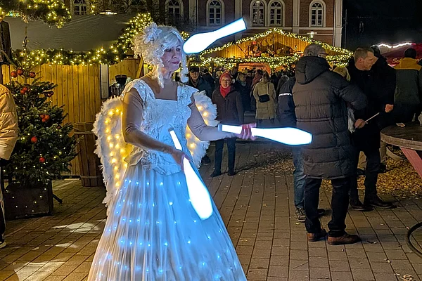 Frau in weißem, mit Lichtern besetztem Kleid jongliert nachts mit leuchtenden Keulen auf einem Weihnachtsmarkt in Bad Segeberg