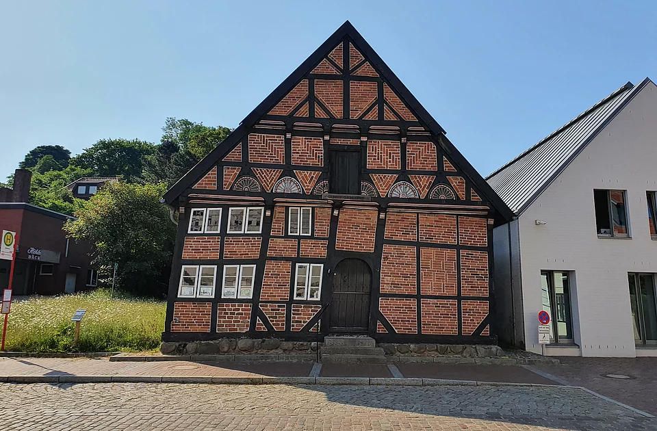 Fachwerkhaus mit Ziegelfüllung und schwarzem Holzrahmen neben modernem weißem Gebäude auf gepflastertem Platz