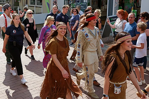 Gruppe von Menschen in historisch inspirierten Kostümen und moderner Kleidung geht auf gepflasterter Straße