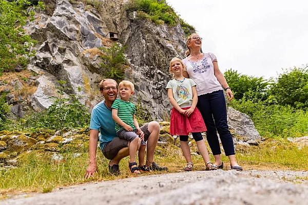 Familie mit zwei Kindern vor dem Kalkberg in Bad Segeberg, Vater kniet, Mutter und Tochter stehen, umgeben von Felsen und Vegetation