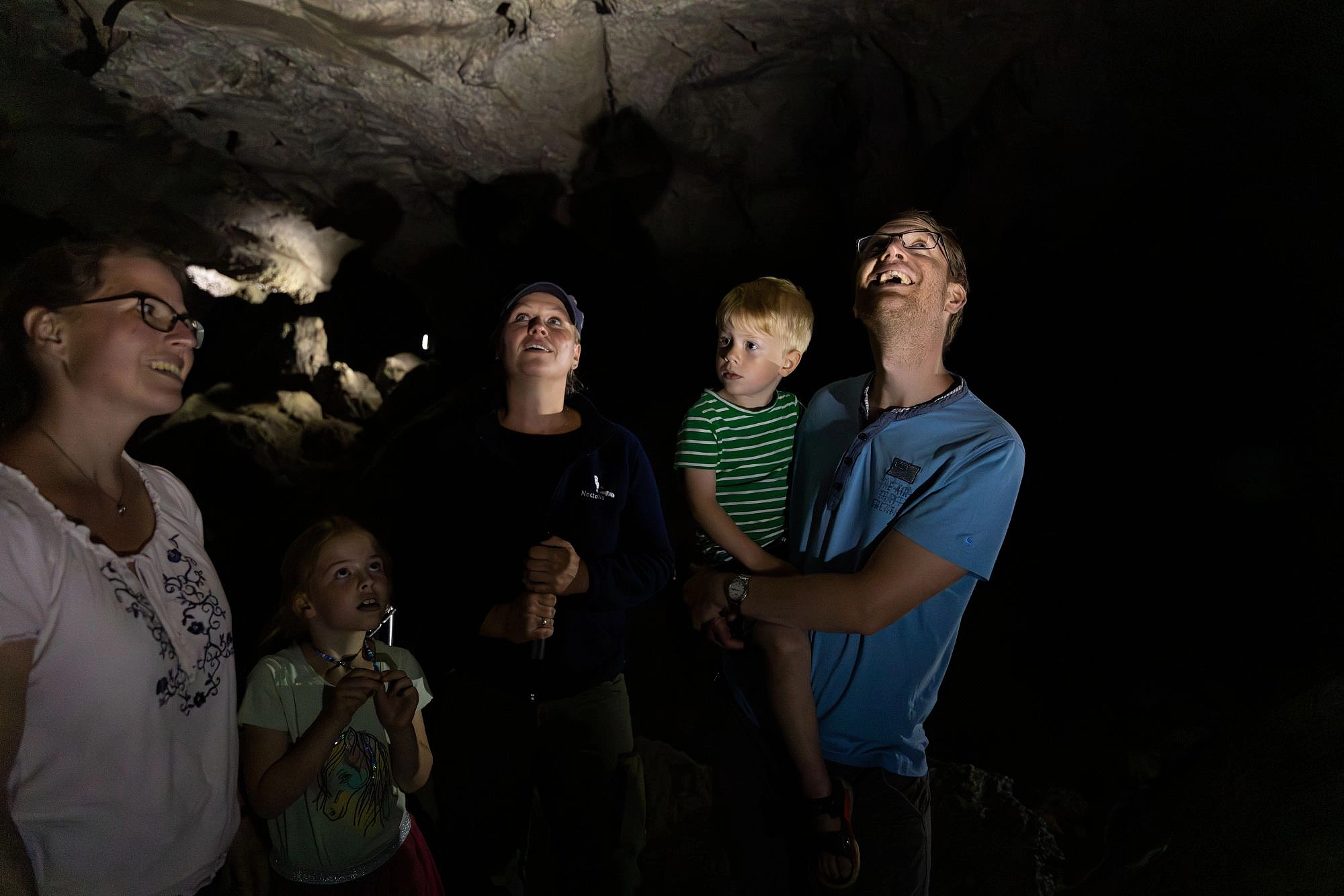 Fünf Personen, darunter zwei Kinder, stehen in einer dunklen Höhle und blicken nach oben
