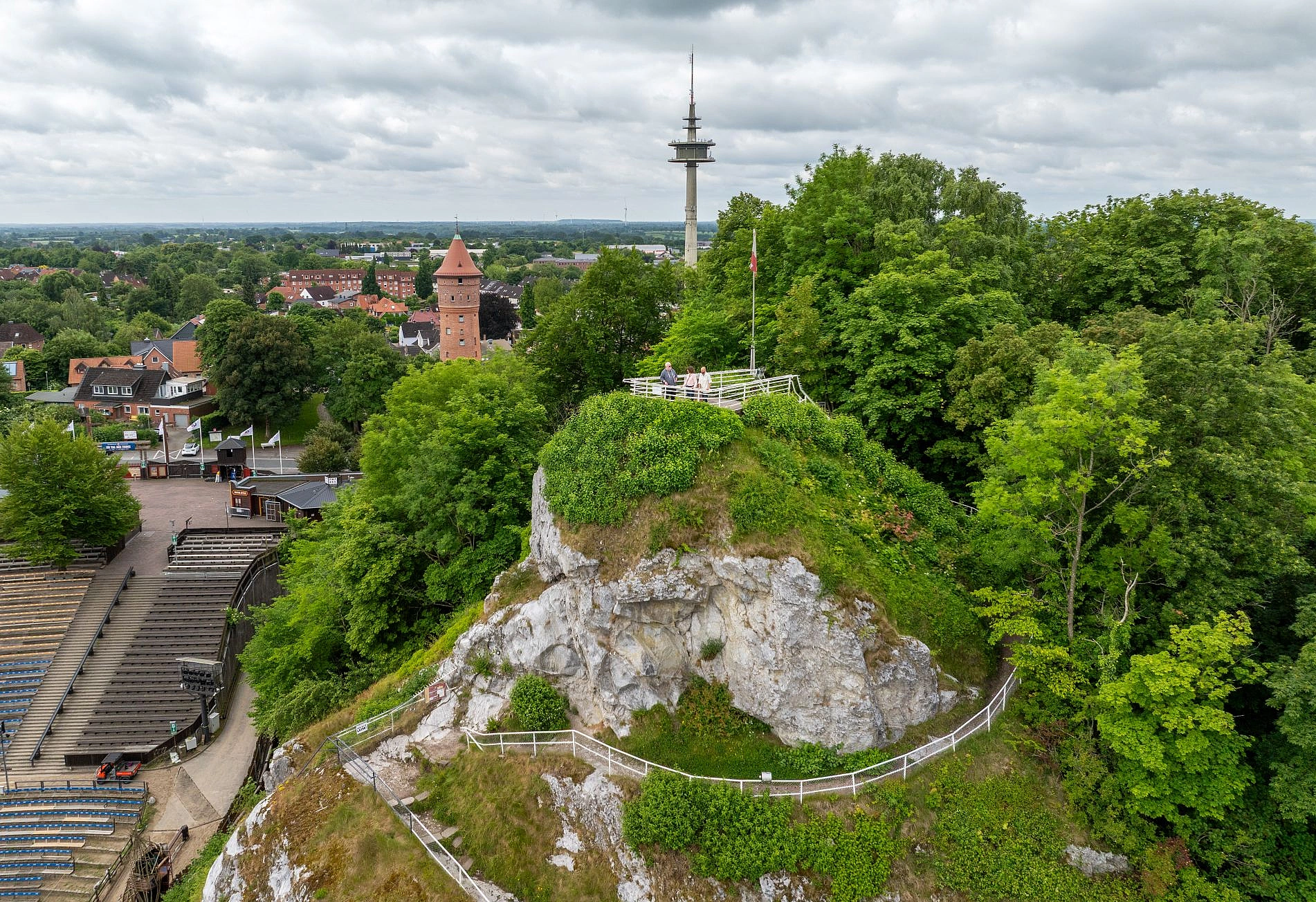 Felsiger Hügel mit Wegen und Geländern umgeben von Bäumen und einer Stadt mit einem Fernsehturm im Hintergrund