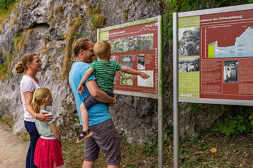 Familie mit zwei Kindern liest Infotafeln am Kalkberg Bad Segeberg vor einer Felswand