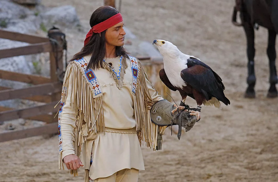 Person in traditioneller Indianerkleidung mit Fransen und Perlenstickerei hält einen Adler auf dem behandschuhten Arm
