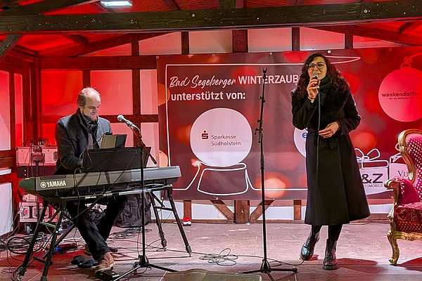 Musiker am Keyboard und Sängerin auf einer weihnachtlich geschmückten Bühne bei einer Veranstaltung in Bad Segeberg