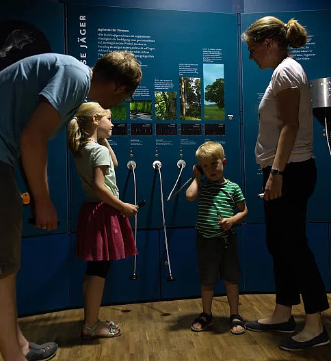 Familie mit zwei Kindern steht vor interaktiven Ausstellungstafeln in der Erlebnisausstellung Noctalis Bad Segeberg