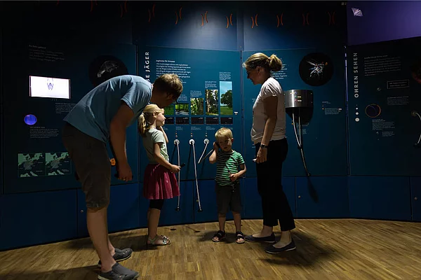 Familie mit zwei Kindern steht vor interaktiven Ausstellungstafeln in der Erlebnisausstellung Noctalis Bad Segeberg