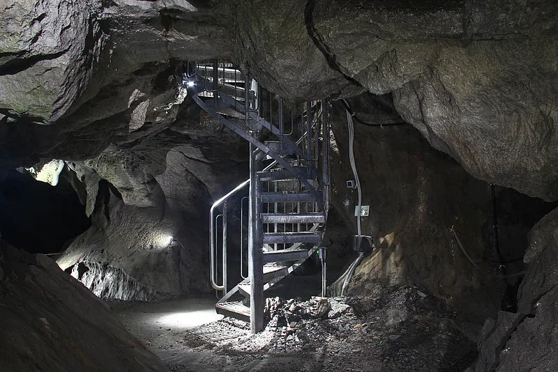 Spindeltreppe aus Metall in einer natürlichen Kalksteinhöhle mit unregelmäßigen Felswänden und installierter Beleuchtung