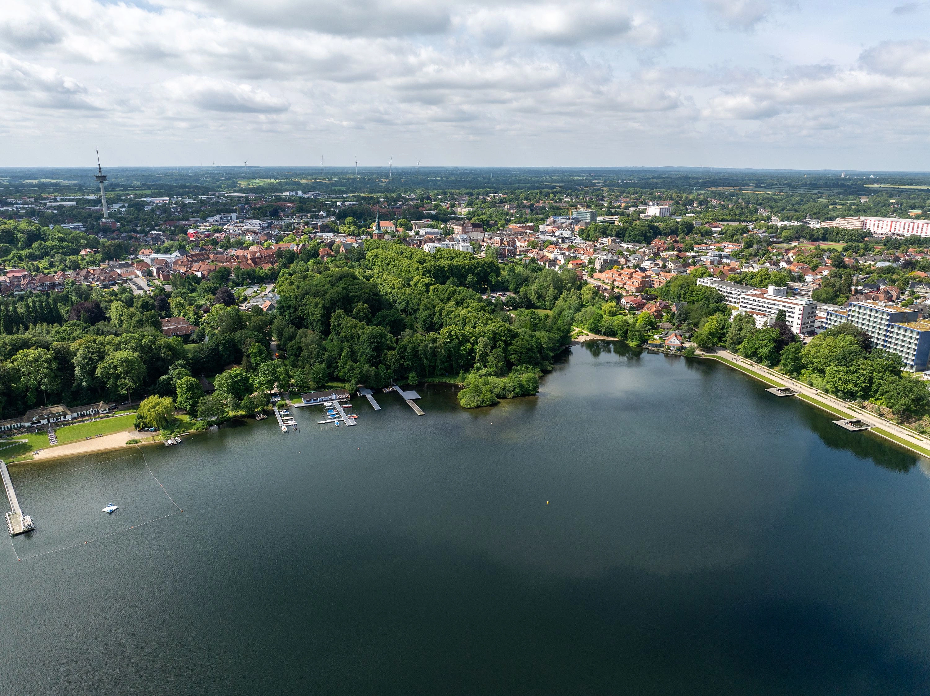 Luftaufnahme eines Sees mit Stegen, umgeben von Bäumen und Wohngebäuden in einer Stadtlandschaft