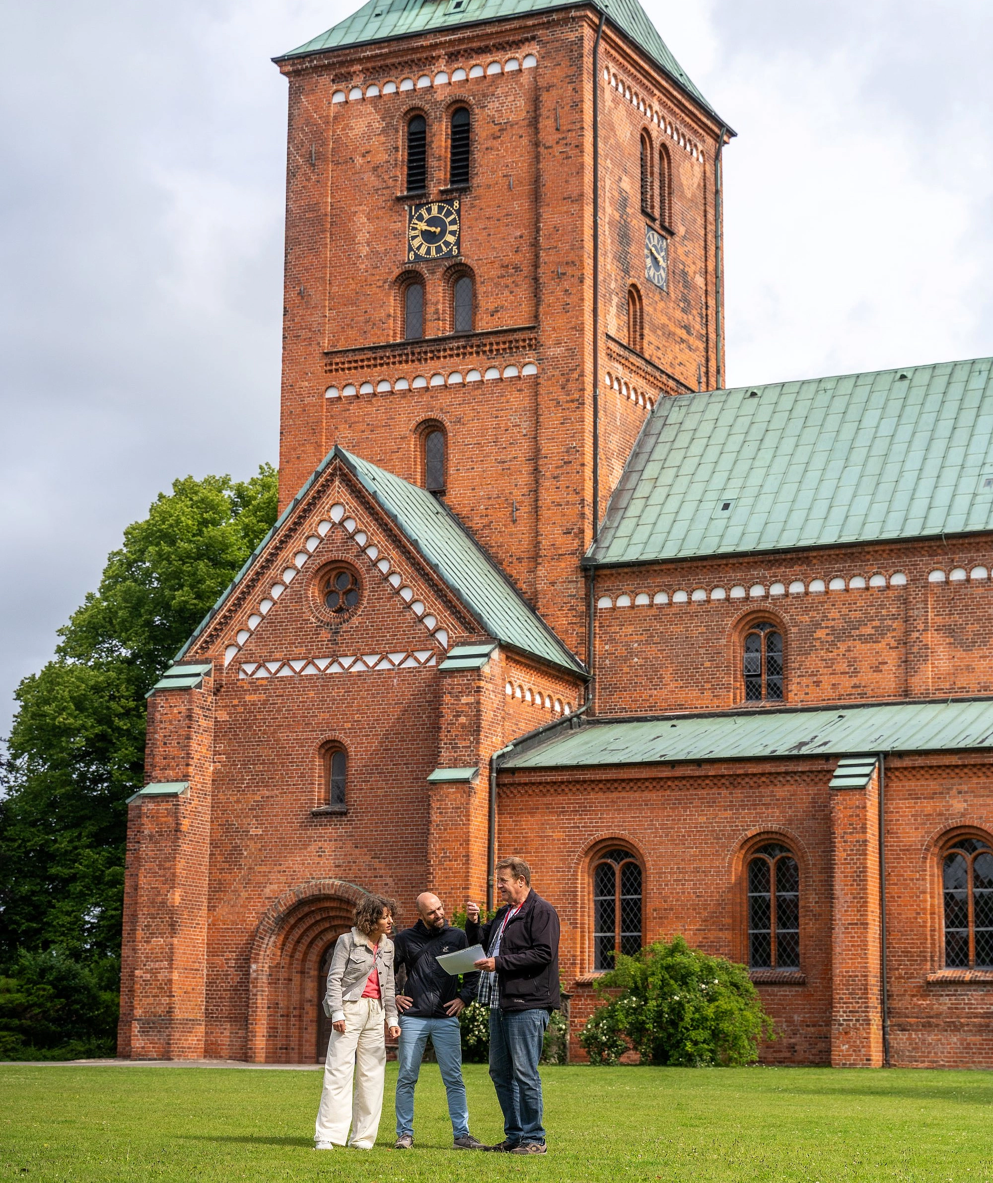 Drei Personen stehen auf einer grüen Wiese vor einer Kirche