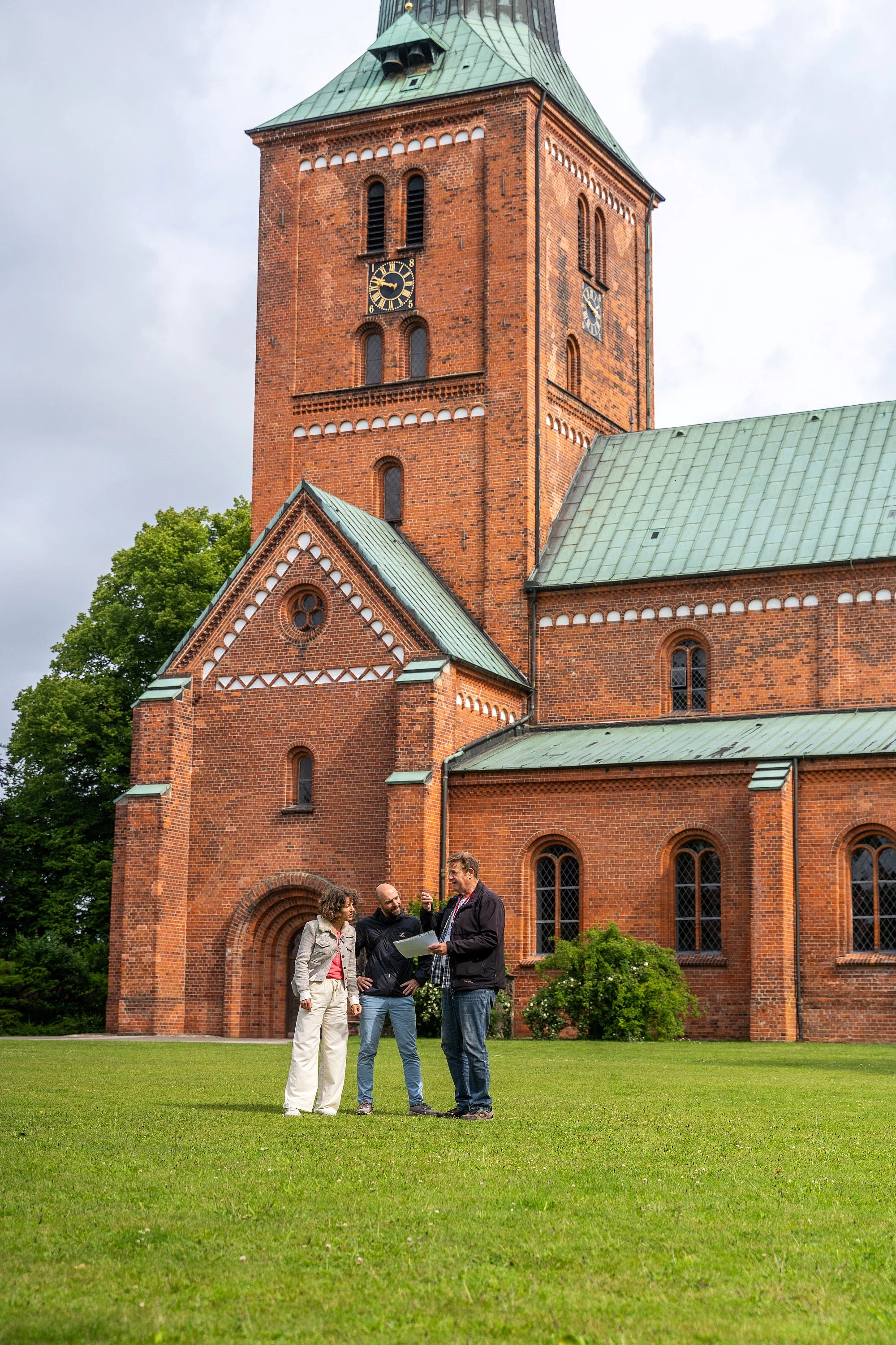 Drei Personen stehen auf einer grüen Wiese vor einer Kirche