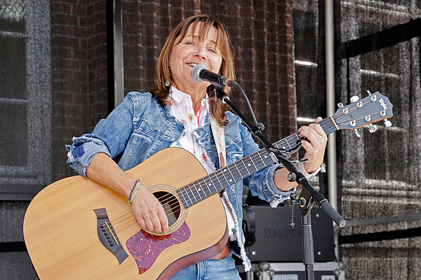 Lächelnde Frau spielt akustische Gitarre und singt vor Mikrofon auf Bühne