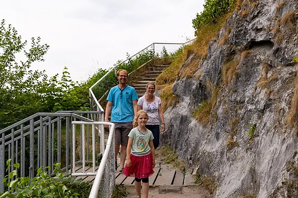 Drei Personen gehen auf einem Weg neben einer steilen Felswand mit Geländer am Kalkberg Bad Segeberg