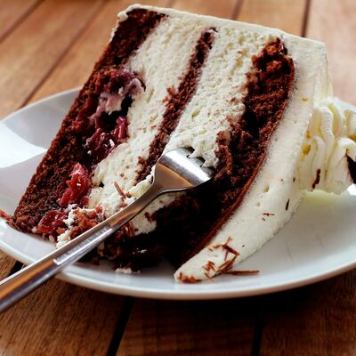 Bild vergrößern: Ein Stück Sahnetorte liegt auf die Seite gekippt auf einem Teller. In der Torte steckt eine Kuchengabel.